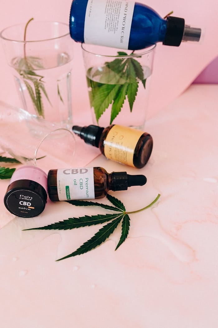 Stylish flat lay featuring CBD oil bottles and hemp leaves on a pink background.